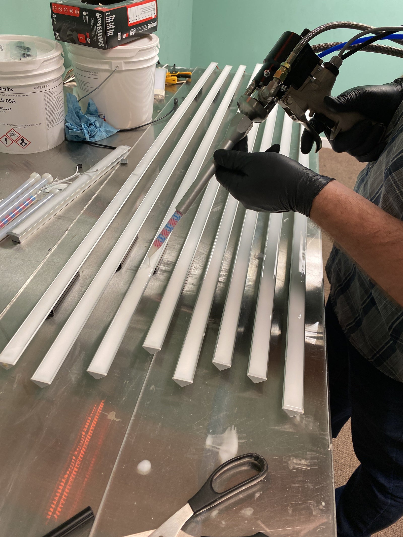 Person applying adhesive or sealant to LED diffuser profiles on a workbench using a dispensing gun, with tools and materials nearby