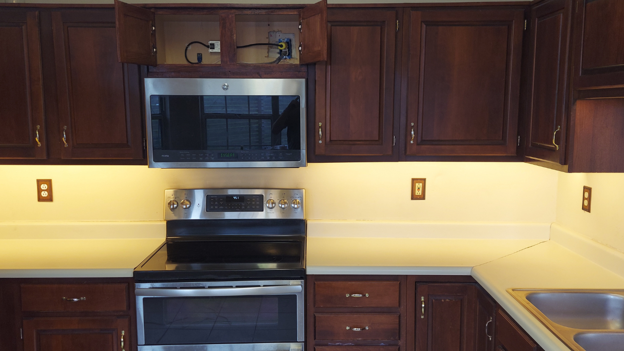 Kitchen with dark wooden cabinets and warm under-cabinet LED lighting installed above the countertops and around the stove