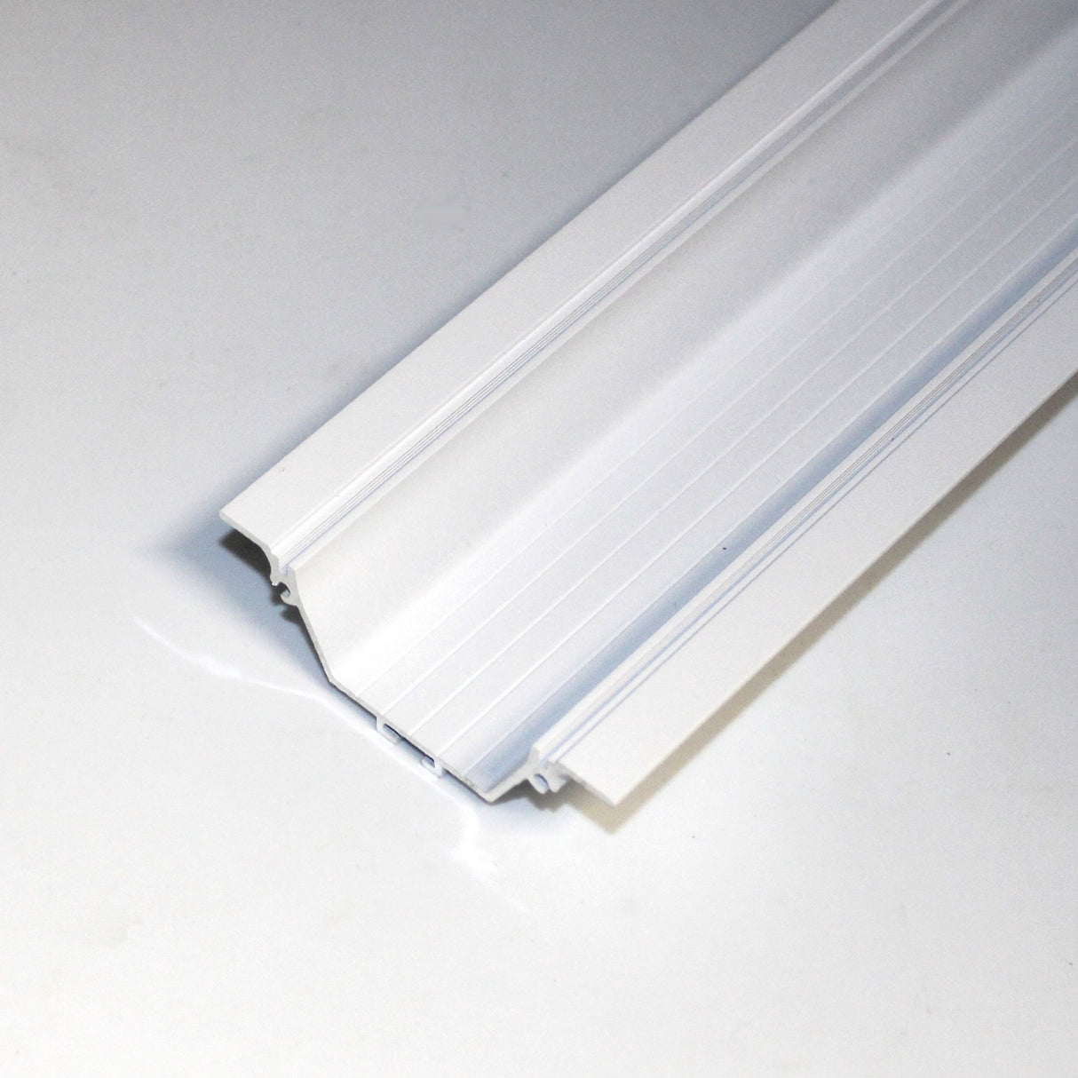 A close-up of the Shallow Ceiling Recessed LED lighting Channel ~ Model Amara shows its angled white profile with grooves, resembling sleek window or door frame molding, placed on a plain white surface.