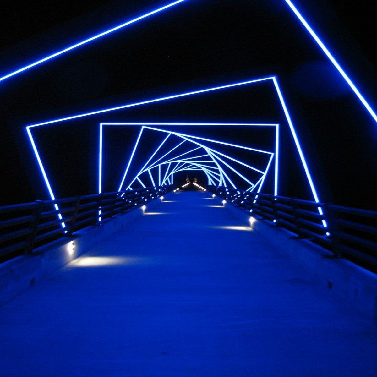 A walkway at night is lit by blue neon square arches using the Flexible LED Neon Light Silicone Profile ~ Model Neon Las Vegas, creating a tunnel effect with geometric patterns against a dark backdrop.