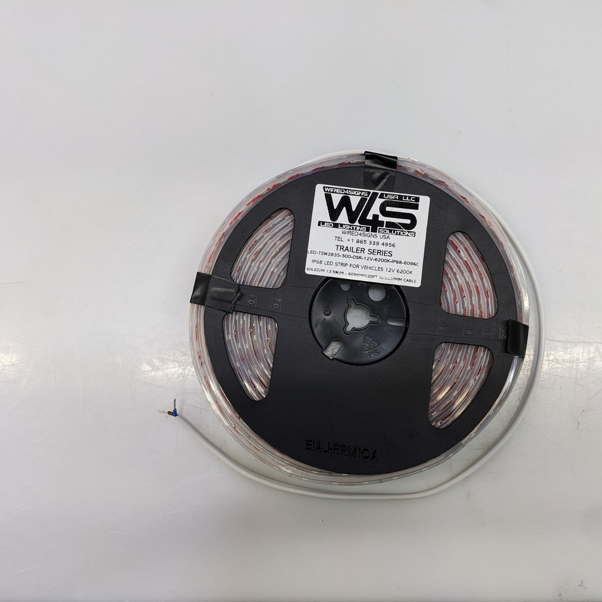 A coiled White IP68 Waterproof LED Strip for Vehicles (12V) ~ Trailer Series sits on a plain white surface, with a black plastic spool and WLS Trailer Series label. One waterproof end is uncoiled, exposing the wires.