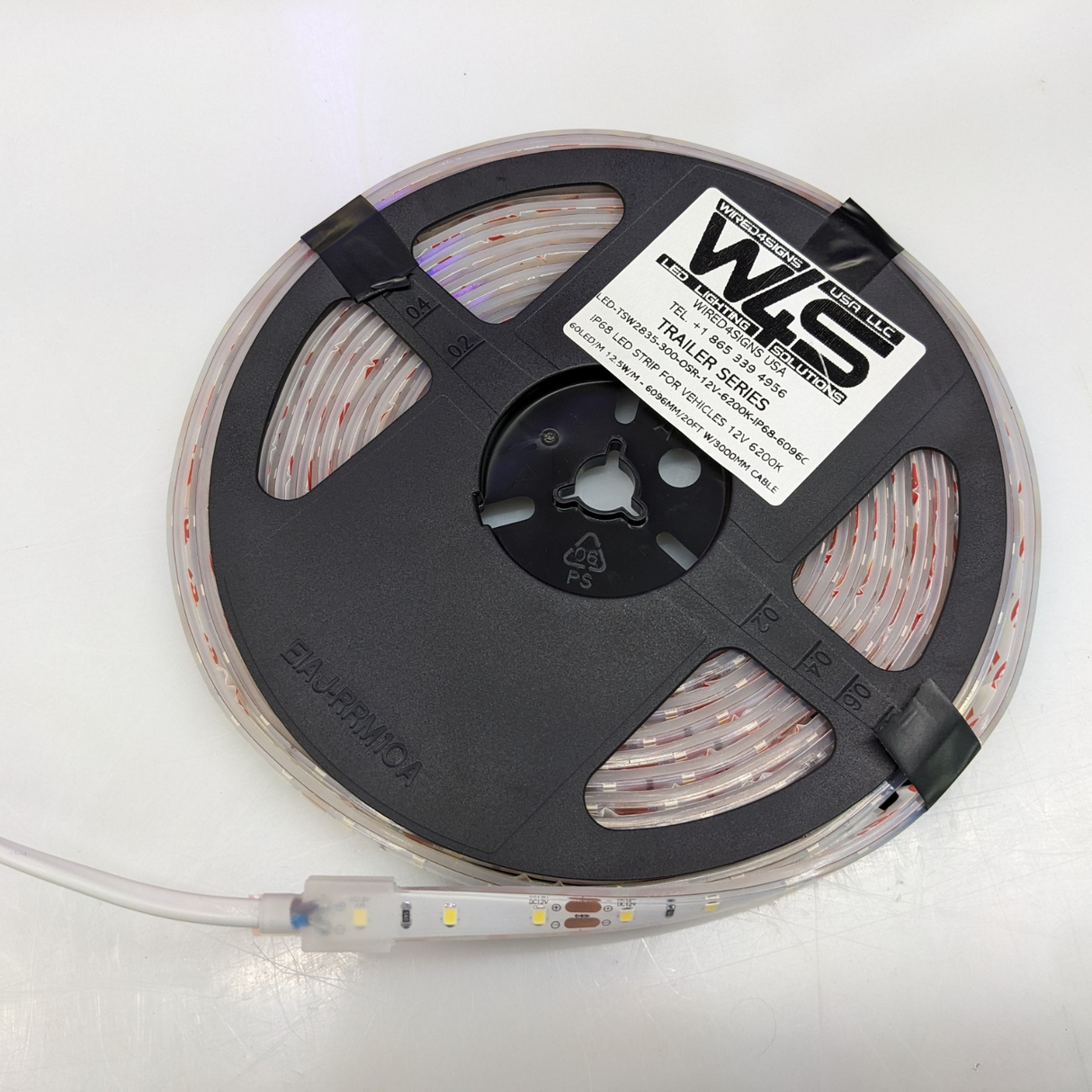 A coiled reel of White IP68 Waterproof LED Strip for Vehicles (12V) ~ Trailer Series features a black spool and white label, with clear, waterproof strip, making it perfect for trailer lights and vehicle LED strip applications.
