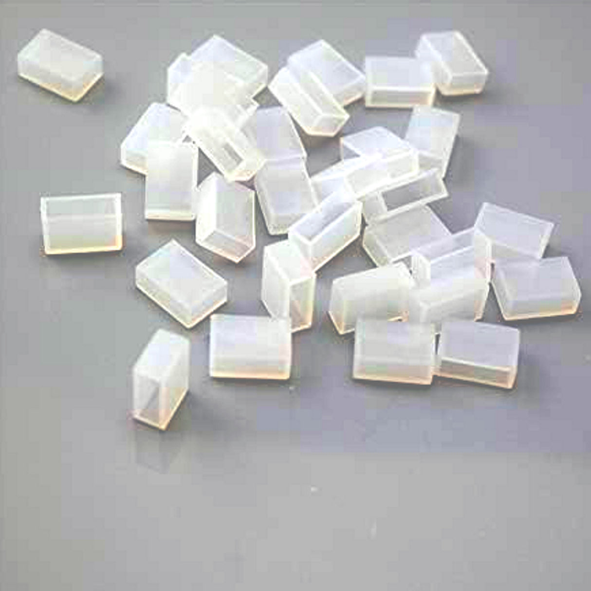 Several small, translucent Waterproof End Cap Covers for IP67/IP68 LED Strips are scattered on a gray surface, perfect for sealing and protecting strip light ends.