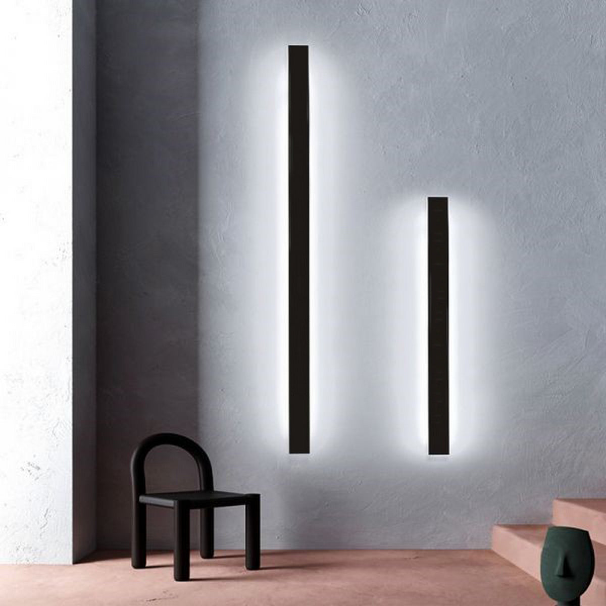 A minimalist interior features a black chair, green-cushioned bench, and two Model New Washington Up & Down Wall Feature Lighting LED Profiles as architectural accents on a light grey textured wall near the pale pink floor and steps.