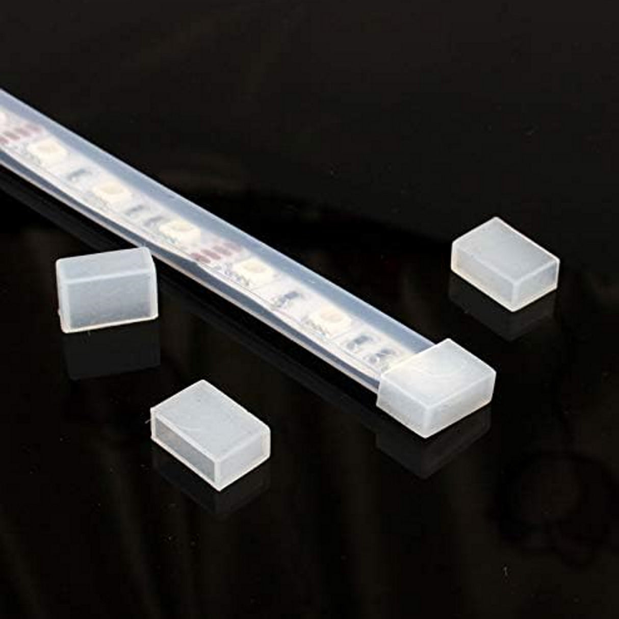 The Waterproof End Cap Cover for IP67/IP68 LED Strip is shown protecting an LED strip’s end, with three extra covers nearby on a glossy black surface for added seal and protection.