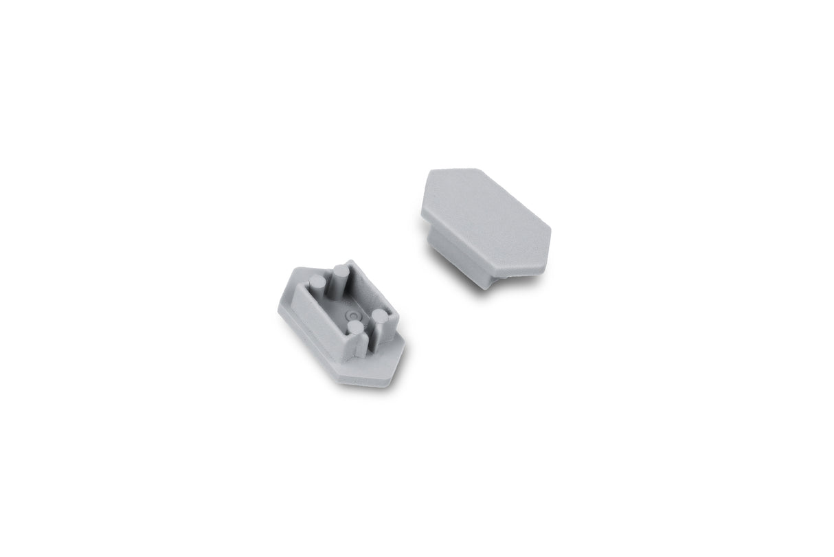 Two small, gray, plastic C End Caps for the Arc12 Duo Profile are displayed on a white background; one is positioned face up showing its prongs, while the other lies face down revealing a flat surface. These components serve as end caps for the Arc12 Duo Profile lighting fixture.