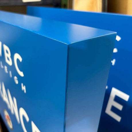 Close-up of a blue, glossy rectangular sign with clean, smooth edges achieved using Cream 2-part Methacrylate Adhesive ~ W4S 55300 (400ml 1:1 Mix / C-System); another similar sign appears in the background.