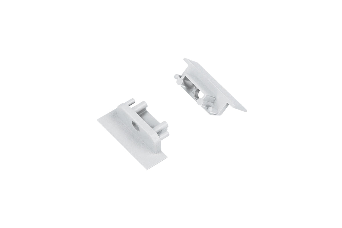 Two small, rectangular, silver metal End Caps for Groove10.v2 Profile with raised edges and cylindrical posts are positioned on a white background facing each other.