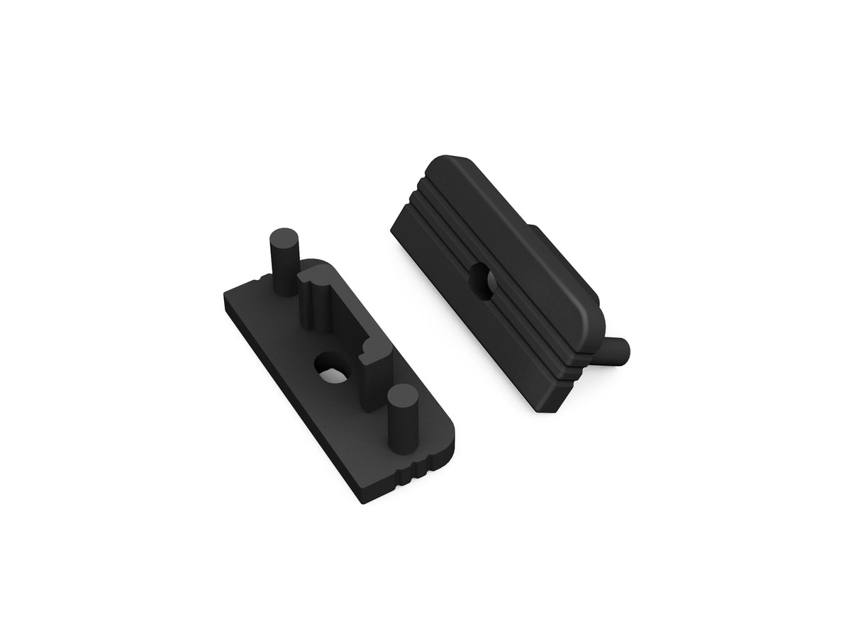 Two black, rectangular plastic End Caps for the Surface10 Profile are displayed on a white background—one lying flat, the other propped upright—to show their ridged surfaces and cylindrical protrusions. Designed with pegs and holes for secure attachment, these versatile LED accessories provide a clean, finished look to your Surface10 LED channel installation.