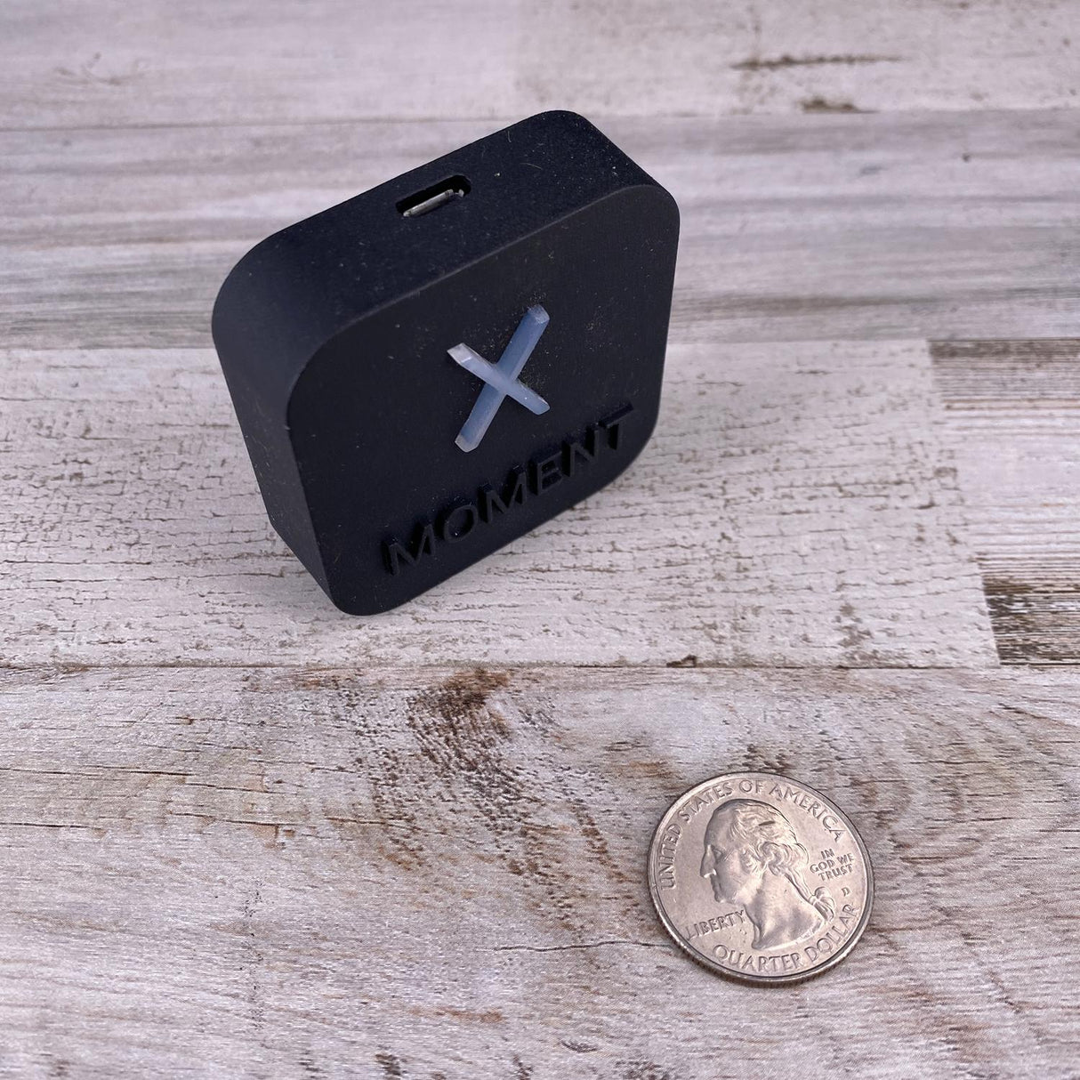 A compact black Casambi Lighting Controller with Alexa Voice Control ~ Estol X-Moment sits on wood next to a U.S. quarter for scale. It features a USB-C port on top and functions as a voice-activated light switch.