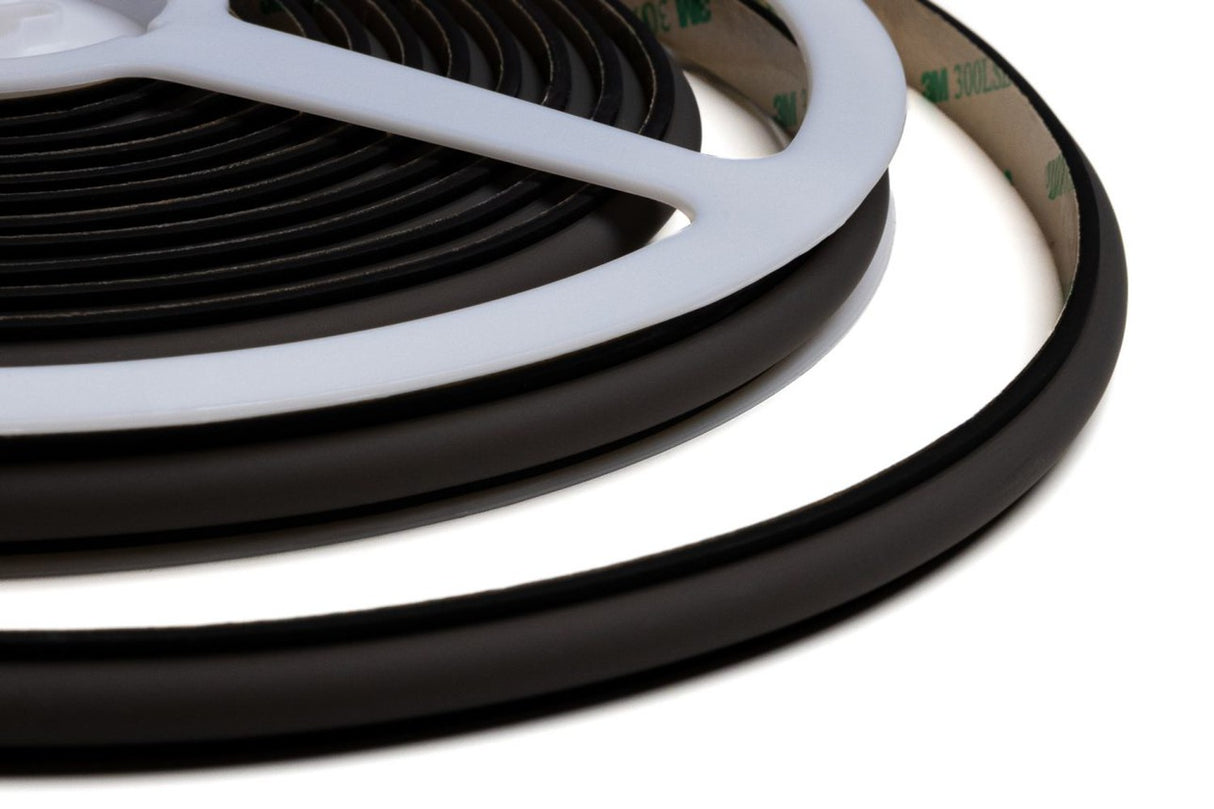 Close-up of a coiled Black IP65 Neon LED Light Line (24V) from the Optimum Black Neon Max Series with adhesive backing, partially covered by a white plastic reel on a white background—ideal for IP65 neon LED installations.