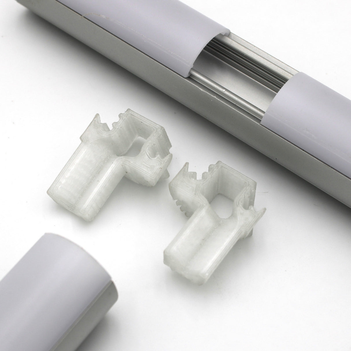 Close-up of two translucent plastic mounting clips, a T Joiner for Alu-Round Profile, and white/metallic Alu-Round profile rail parts on a white background.
