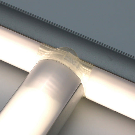 Close-up of a clear plastic T Joiner for Alu-Round Profile connecting two translucent fluorescent light tubes at a right angle, against a pale gray background.