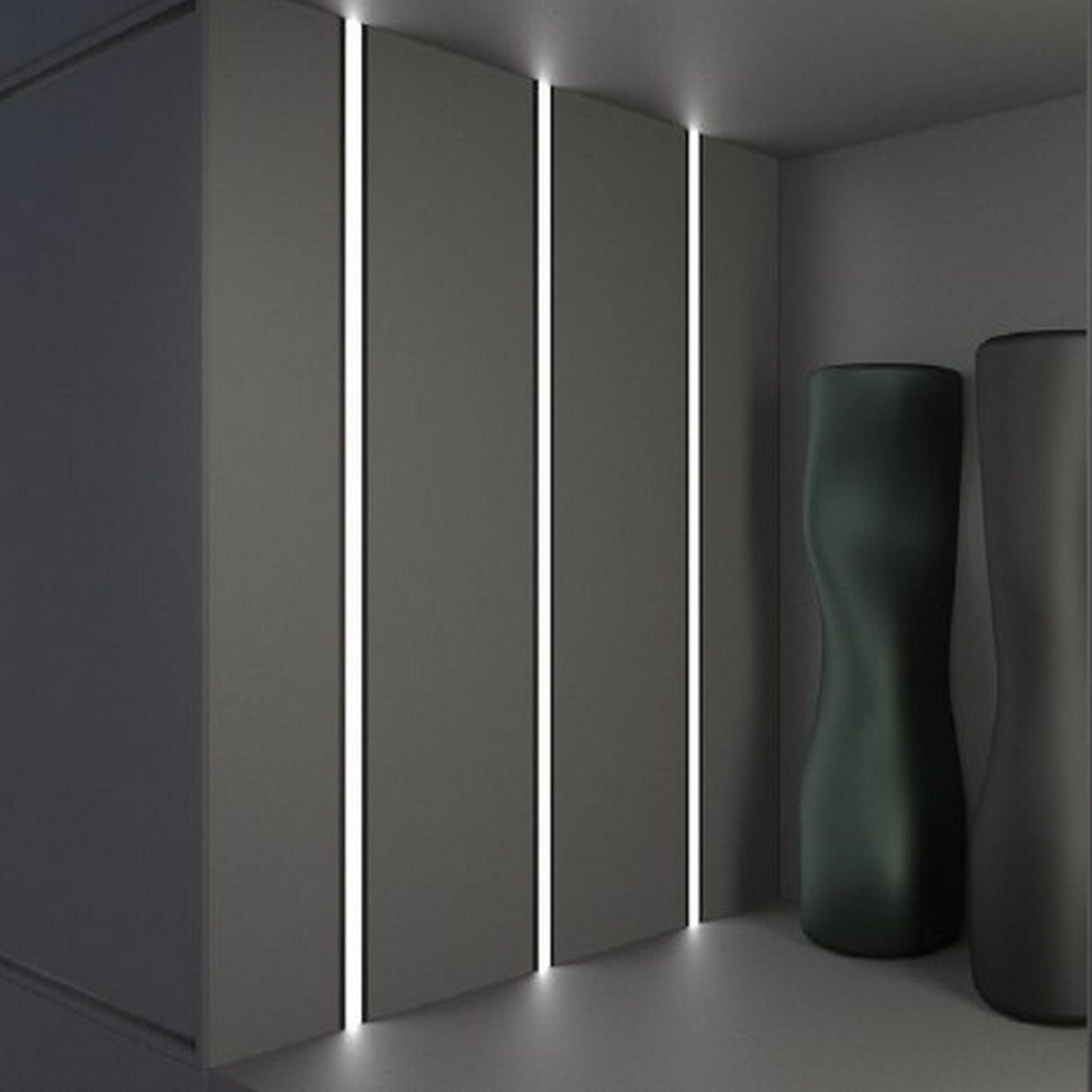 A minimalist room features vertical LED strips set in the 1.3” Deep-Section Recessed LED Channel (Model Vario30-07) on a gray wall and two tall, dark sculptures in the corner, creating a modern, sleek, and uncluttered atmosphere.