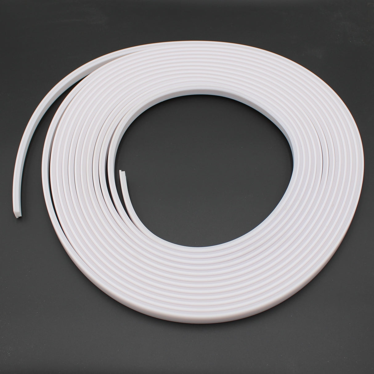 The Arles LED Strip Flexible Diffuser, a coiled strip of white plastic edging designed for flexible diffusion, is displayed in a spiral shape on a dark surface.