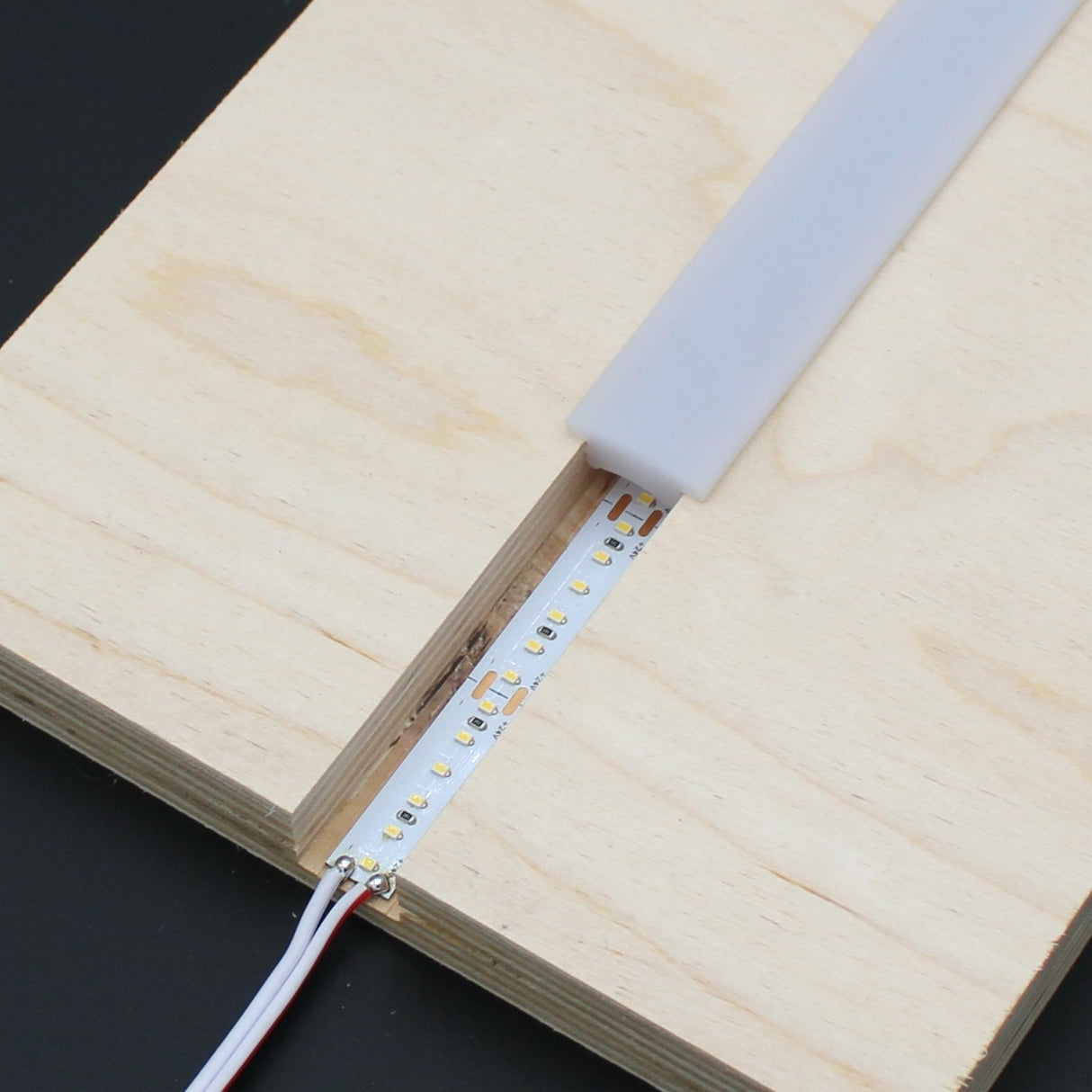 An Arles LED Strip Flexible Diffuser partially covers an LED strip installed in a narrow groove cut into light-colored plywood, with two wires connected to one end of the strip.