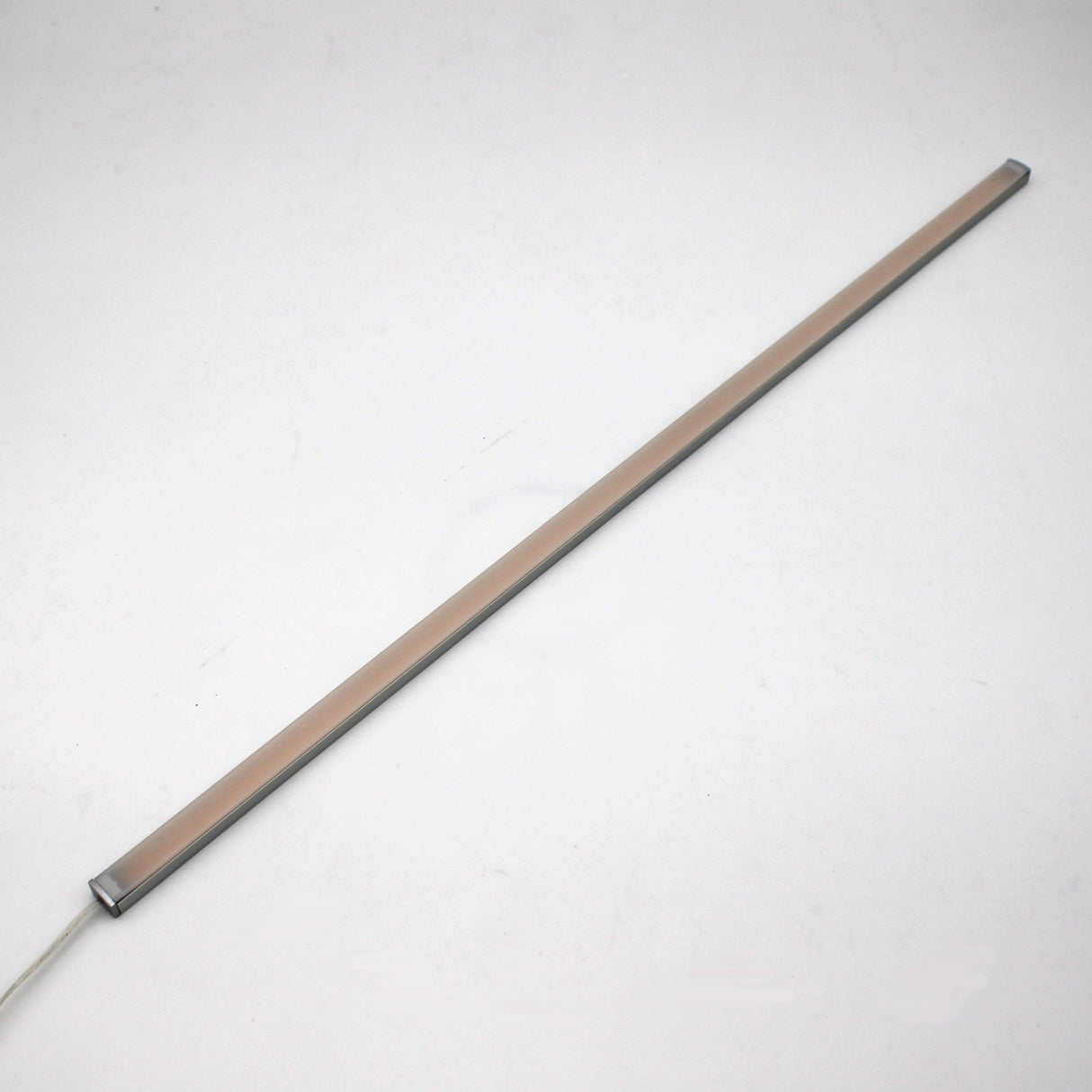 A slim, rectangular White Universal Surface-mount LED Lighting Fixture ~ Begton12 Series with a beige cover is placed diagonally on a plain white background. This dotless light bar features a visible power cord, ideal for under-cabinet lighting.