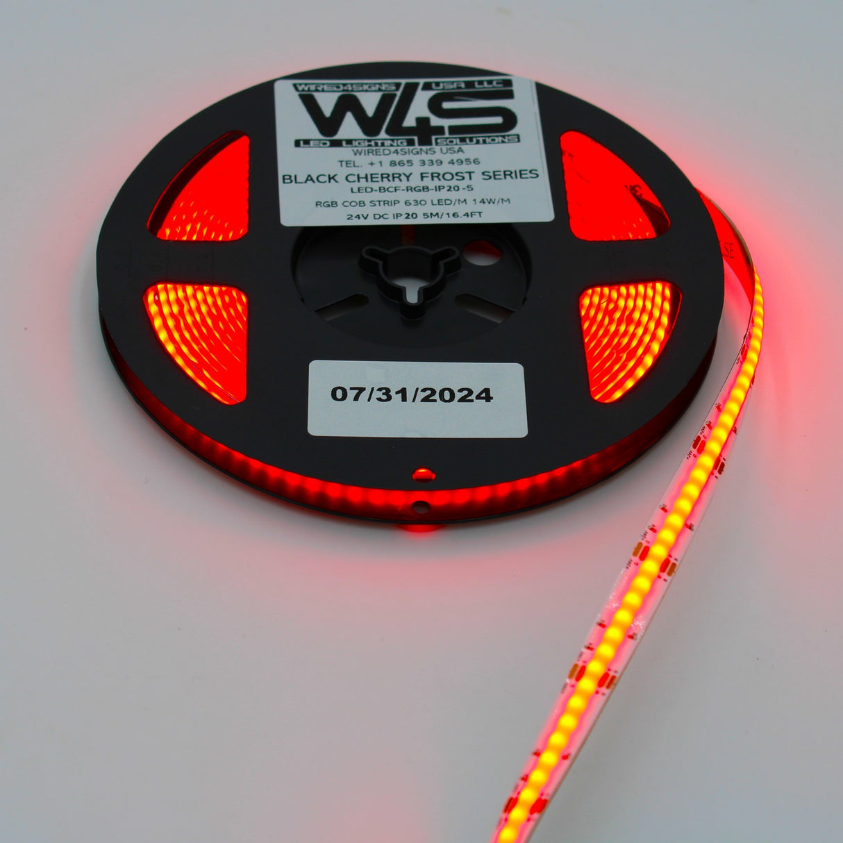 A spool of red-glowing RGB COB IP20 LED Strip (24V) from the Black Cherry Frost Series is partially unrolled, with a label showing “07/31/2024.”.