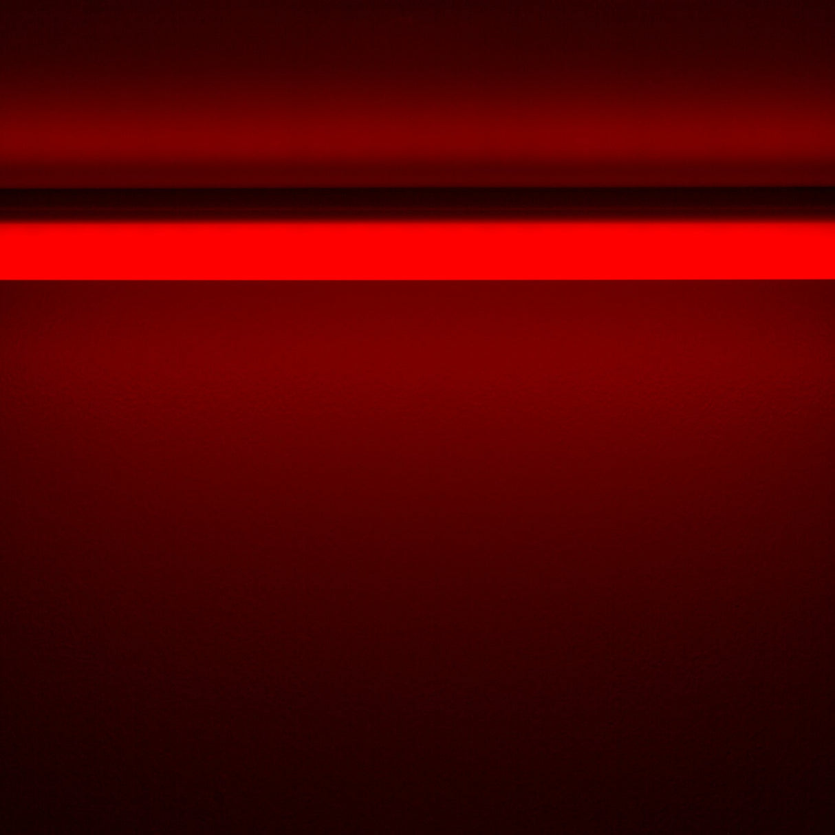 A Colored Border Contour Tube Light ~ Hi-Lite 30 Straight Section glows horizontally near the top of a dark, textured red wall, casting a soft red light below as the lower area fades into deeper red shades.