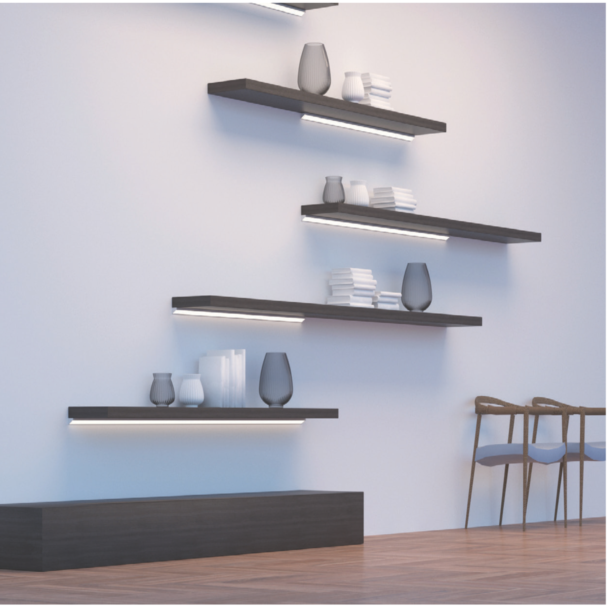Four black shelves with Surface Mount Corner LED Channel ~ Model Corner16 lighting are mounted on a white wall, displaying vases and books. Two modern wooden chairs sit to the right on wooden flooring.