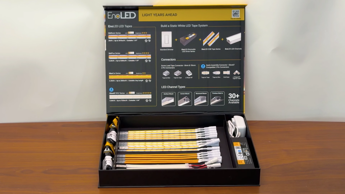 An EnoLED LED Strip Sample Box is open on a table, displaying multiple yellow LED strips, connectors, power adapters, and an instruction guide inside the box lid.