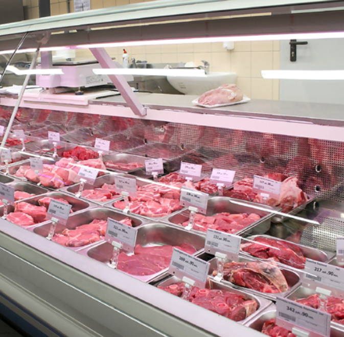 A supermarket meat display case is brightly illuminated by the FLX Stix CDV Series Commercial Refrigerator Lighting LED System, showcasing assorted raw red meat cuts arranged in metal trays with clear price tags for optimal freshness.