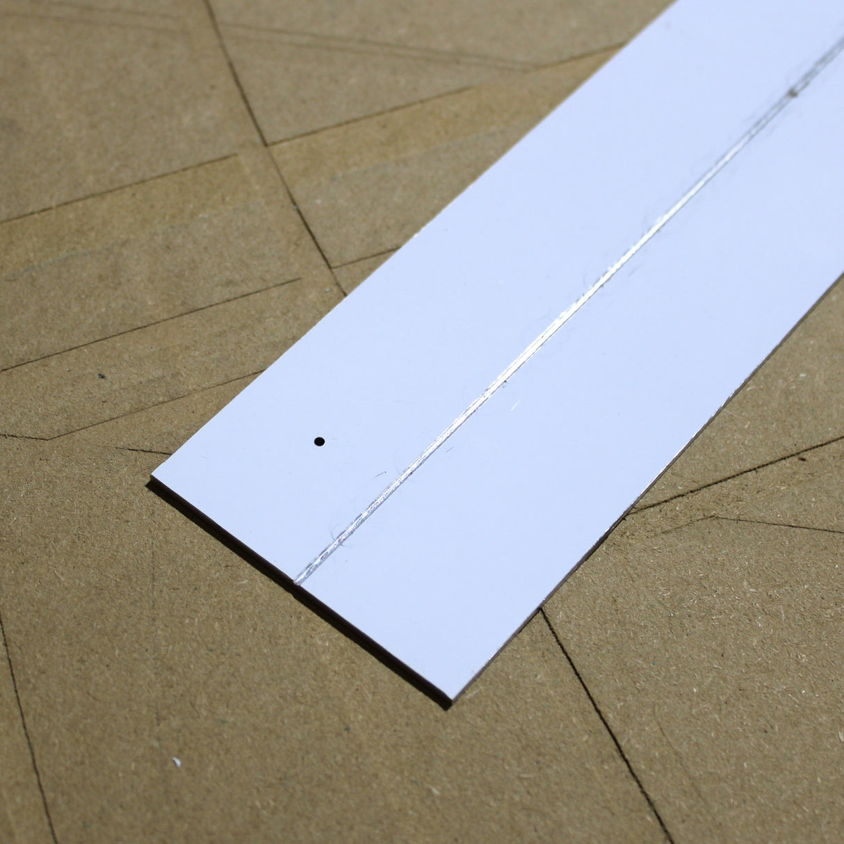An Aluminum Heatsink for Holston74 Profile, featuring a white rectangular design with a thin silver line and a small hole near one end, rests on brown cardboard with faint pencil markings.