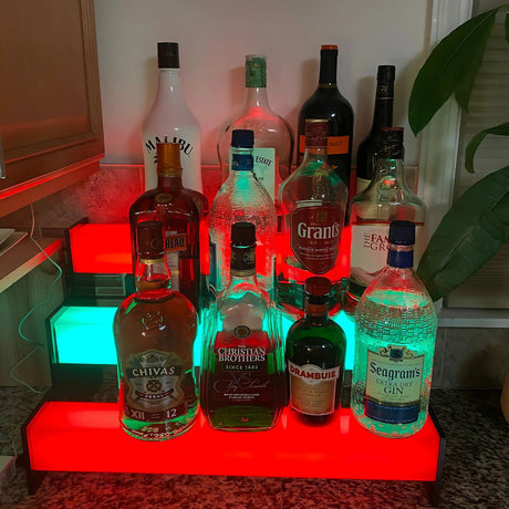 A variety of liquor bottles are displayed on red and green shelves with an RGB pixel LED strip using the 2.91 Square Polycarbonate LED Lighting Tube ~ Model Holston74, set on a kitchen countertop. A large plant sits to the right.