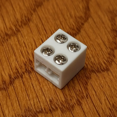 A 2-Pin Solderless LED Strip Light Screw Connector with screw-fastening is shown on a brown wood surface.