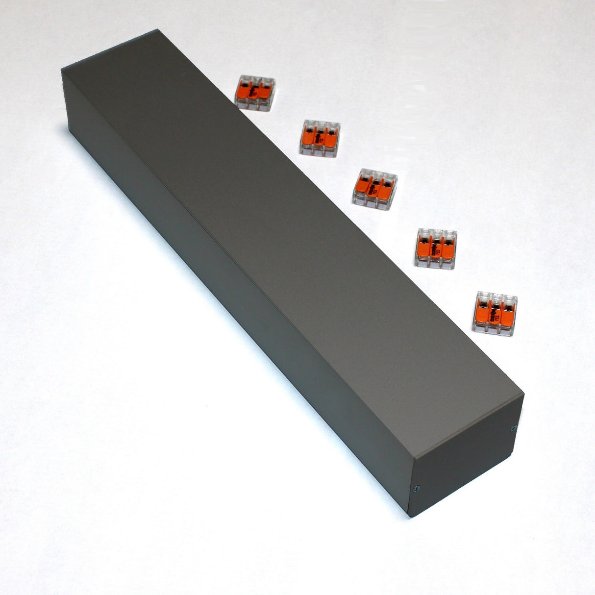 A long, rectangular, dark gray Custom PL55 J-Box sits on a white surface. Six clear plastic electrical connectors with orange levers are arranged beside it, ready for secure electrical connections.