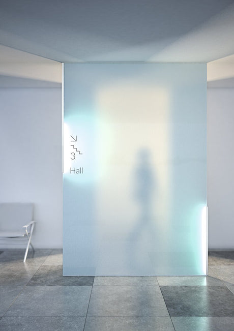 A blurred silhouette appears through a 3/8 glass wall illuminated by the Klus KRAV-810 Edge-lit LED Extrusion in a modern interior; a chair is to the left, with signage pointing to third-floor stairs and hall.