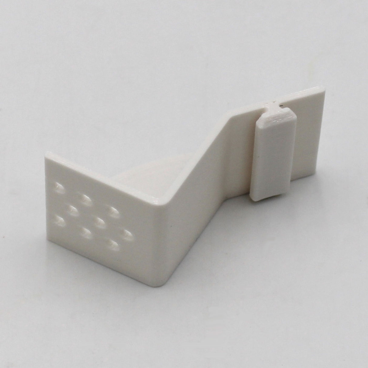 The Plastic Mounting Bracket for Caracas Profile is a small, white, Z-shaped 3D printed bracket with a peg and textured dots on one side, shown against a plain white background. Available from Wired4signs USA.