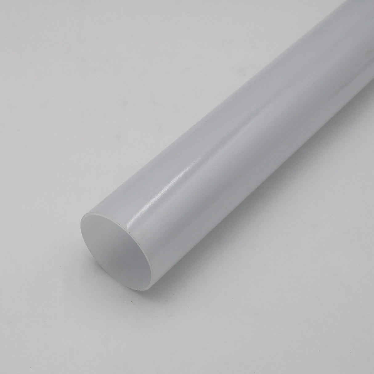 A close-up of a Diffuser for 360 Degree suspended LED Channel - ALU360, plain and white, lying diagonally on a smooth, light grey surface.