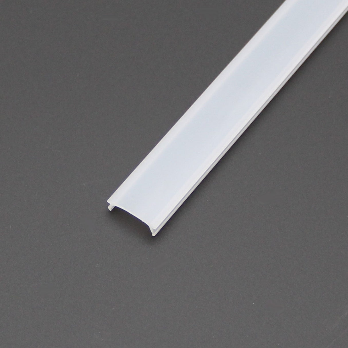 A white, semi-transparent diffuser with a curved top and open sides is placed diagonally on a dark gray surface. This rectangular plastic cover fits SLW8, RSLW8, SLW15, RO38, and Wall LED Lamp series profiles for housing LED strip lights.