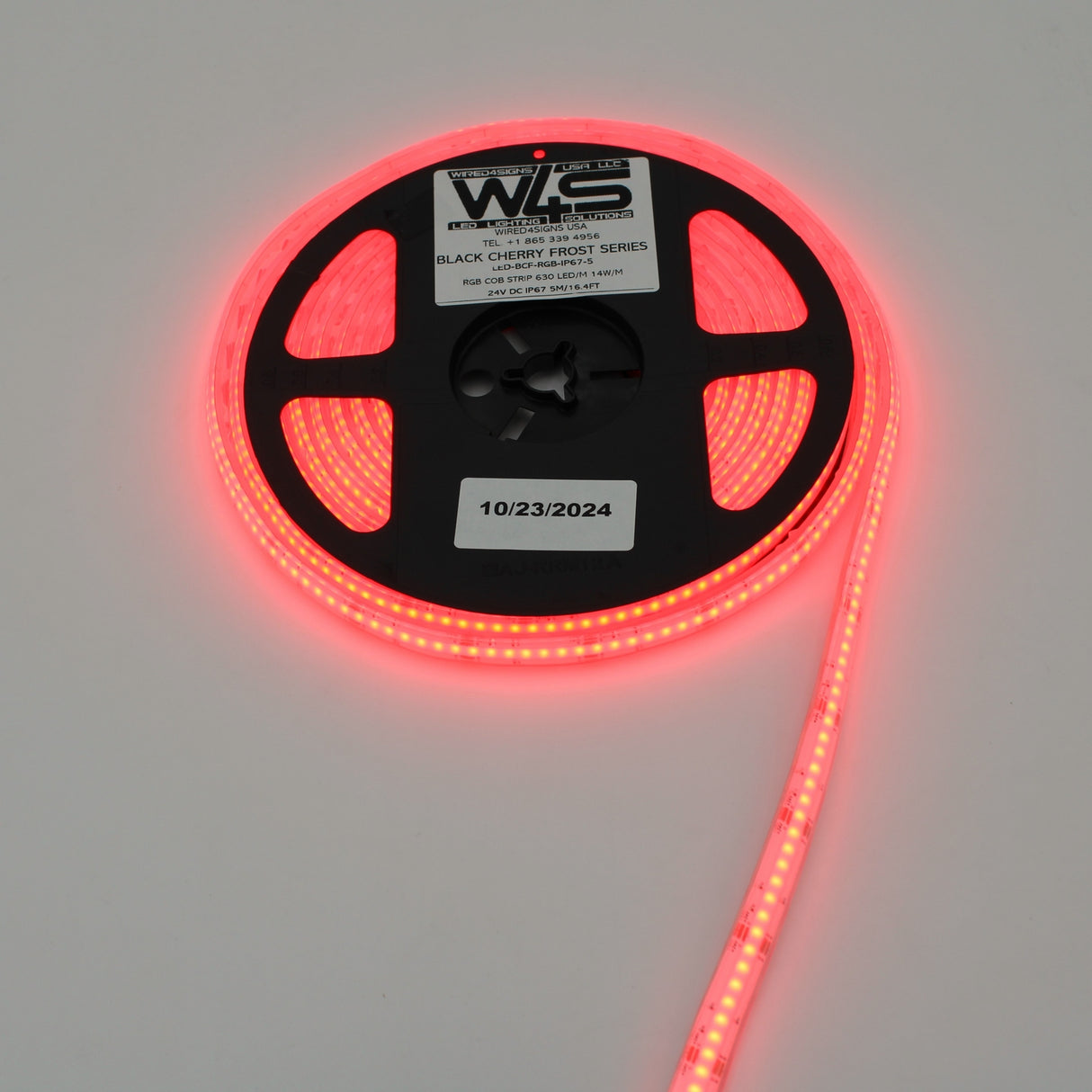 A spool of RGB COB IP67 LED Strip (24V) from the Black Cherry Frost Series glows brightly on a white background. The reel features product information and a sticker dated 10/23/2024.