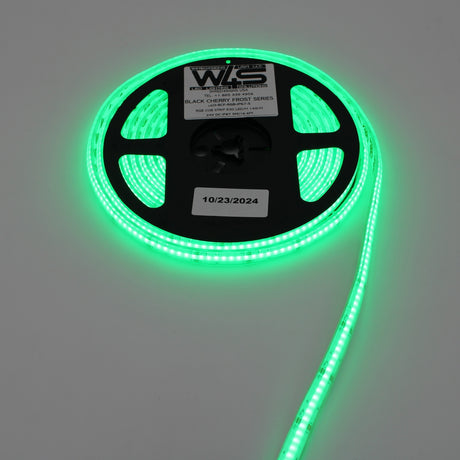 A spool of RGB COB IP67 LED Strip (24V) ~ Black Cherry Frost Series glows green on a white surface, with a label and a sticker showing the date 10/23/2024.
