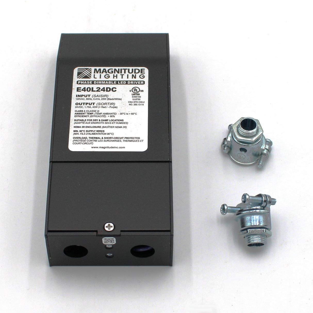 A black Dimmable Class 2 Electronic LED Driver (24V) ~ Magnitude E Series with a white label sits on a white surface beside two metal cable connectors. The label shows input/output info and supports phase dimming or TRIAC controls.