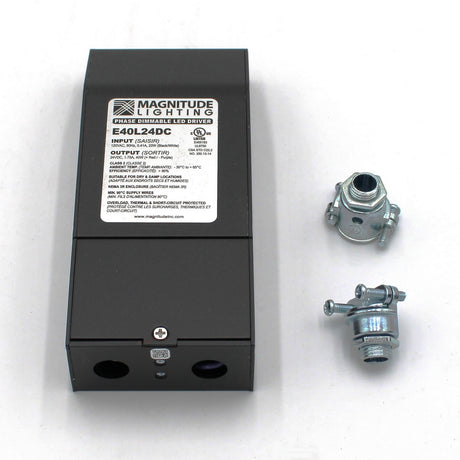 A black Dimmable Class 2 Electronic LED Driver (24V) ~ Magnitude E Series with a white label sits on a white surface beside two metal cable connectors. The label shows input/output info and supports phase dimming or TRIAC controls.