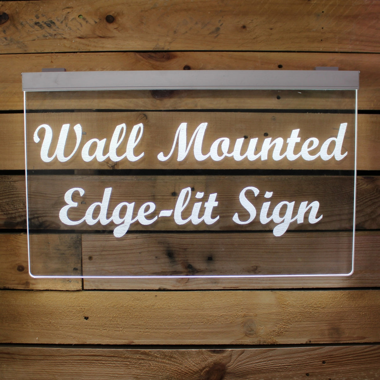A glowing, rectangular, wall-mounted Edge-lit Acrylic Sign Base Channel ~ Model Hannover features white script on acrylic, displayed against a wooden plank wall and illuminated by hidden LED strips.