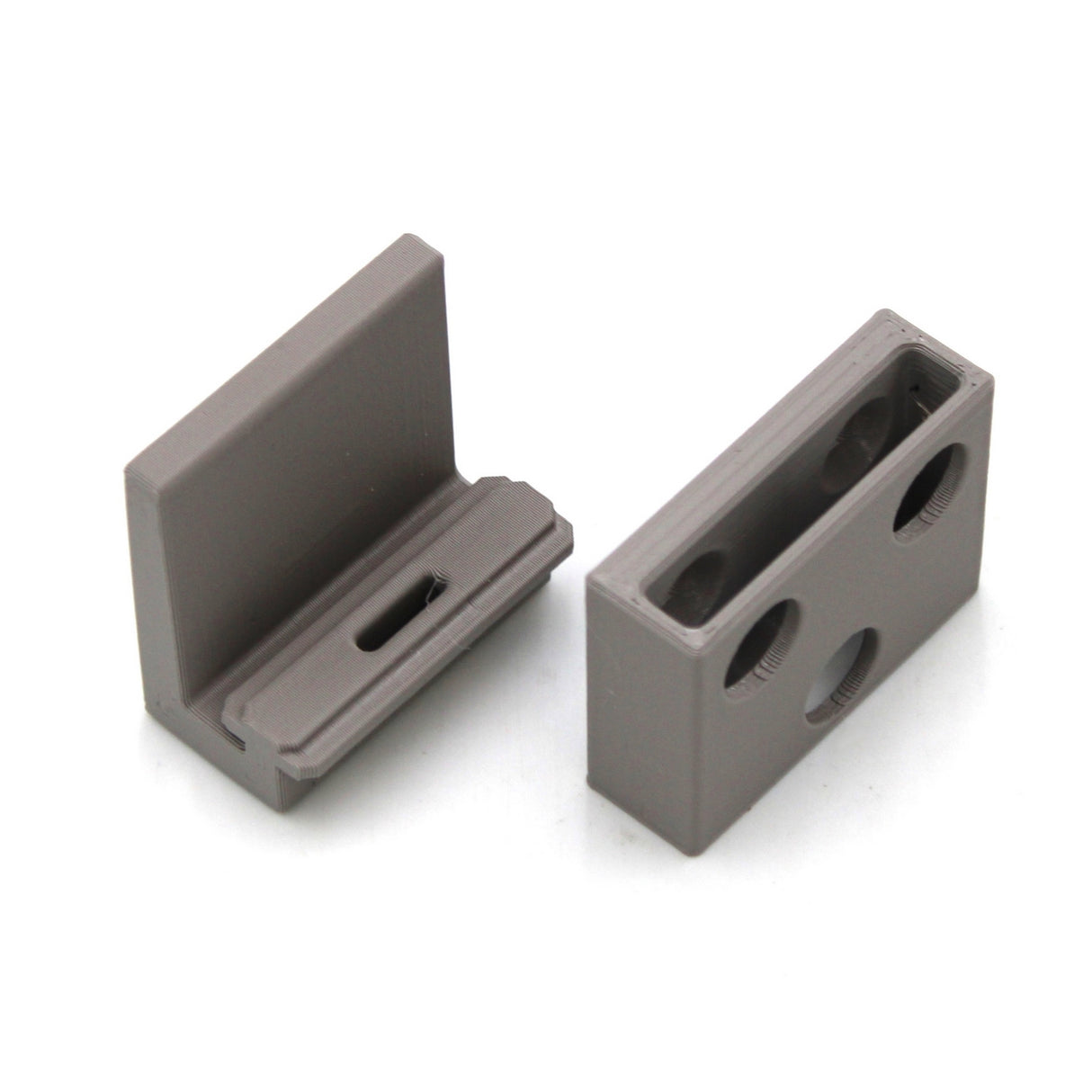 Two gray, L-shaped Wall Mounting Brackets for Hannover Profile with holes and slots are shown on a white background. One stands upright and the other lies flat, highlighting features ideal for supporting edge-lit acrylic signage.