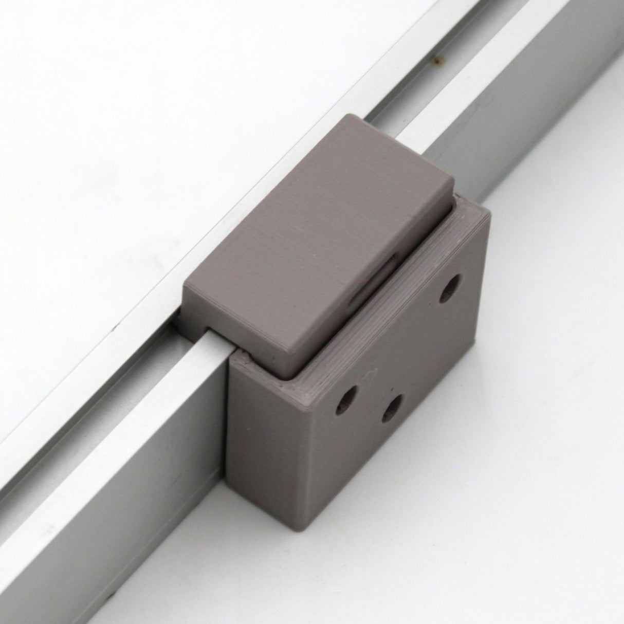 A close-up of the Wall Mounting Bracket for Hannover Profile, featuring a gray rectangular slider on a silver metal rail with two front screw holes—ideal for secure and precise installations.