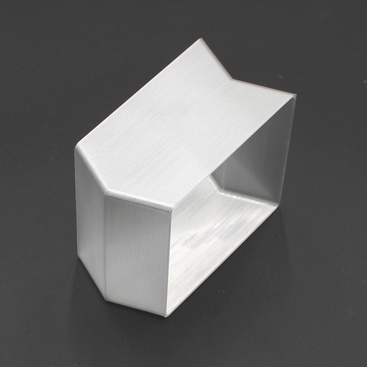 A translucent elbow designed for the Holston74 profile rests on a dark surface. Rectangular with angled top edges, it’s hollow with open front and back, giving it a modern, geometric look.