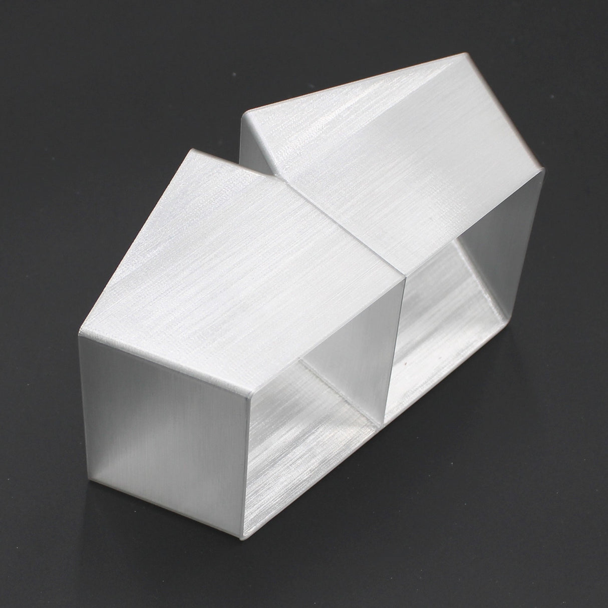 Two geometric, brushed silver Holston74 profile housings are joined side by side with a Translucent Elbow for Holston74 Profile, forming an abstract modern design against a black background.