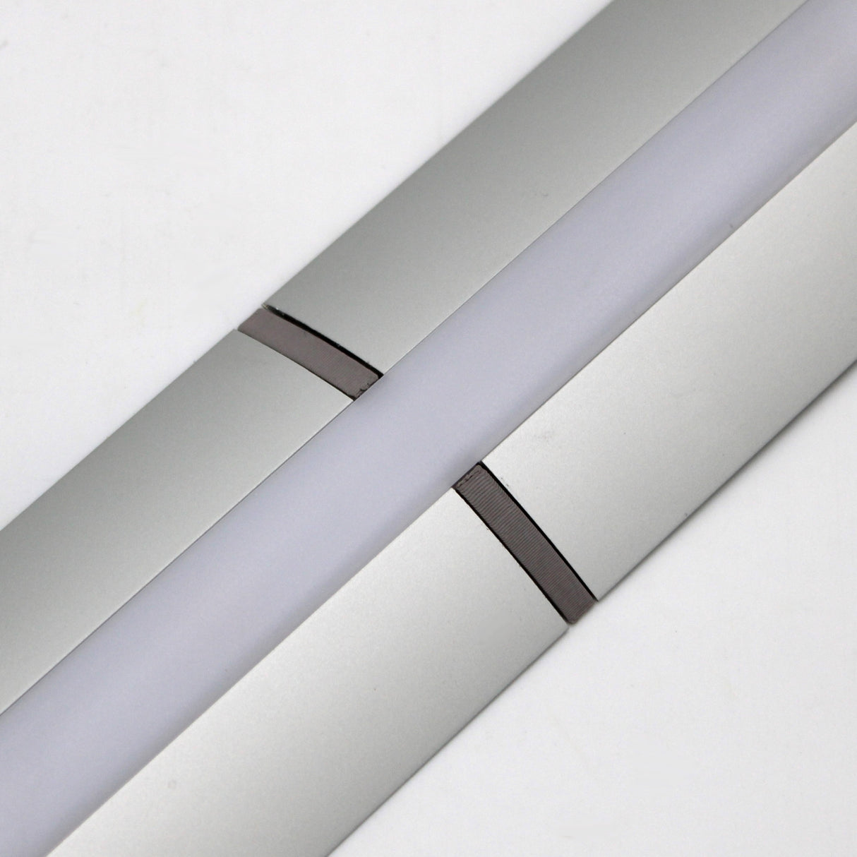 Close-up of a Plastic Straight Connector for Alu-Flat Profile, shown with a modern silver LED light fixture and white diffuser, set diagonally against a plain white background.