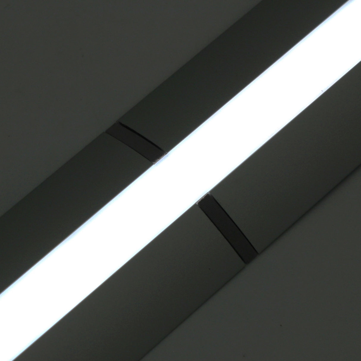 A close-up view of a bright LED light with a metallic Alu-Flat profile frame, mounted at an angle against a dark background, joined using the Plastic Straight Connector for Alu-Flat Profile.