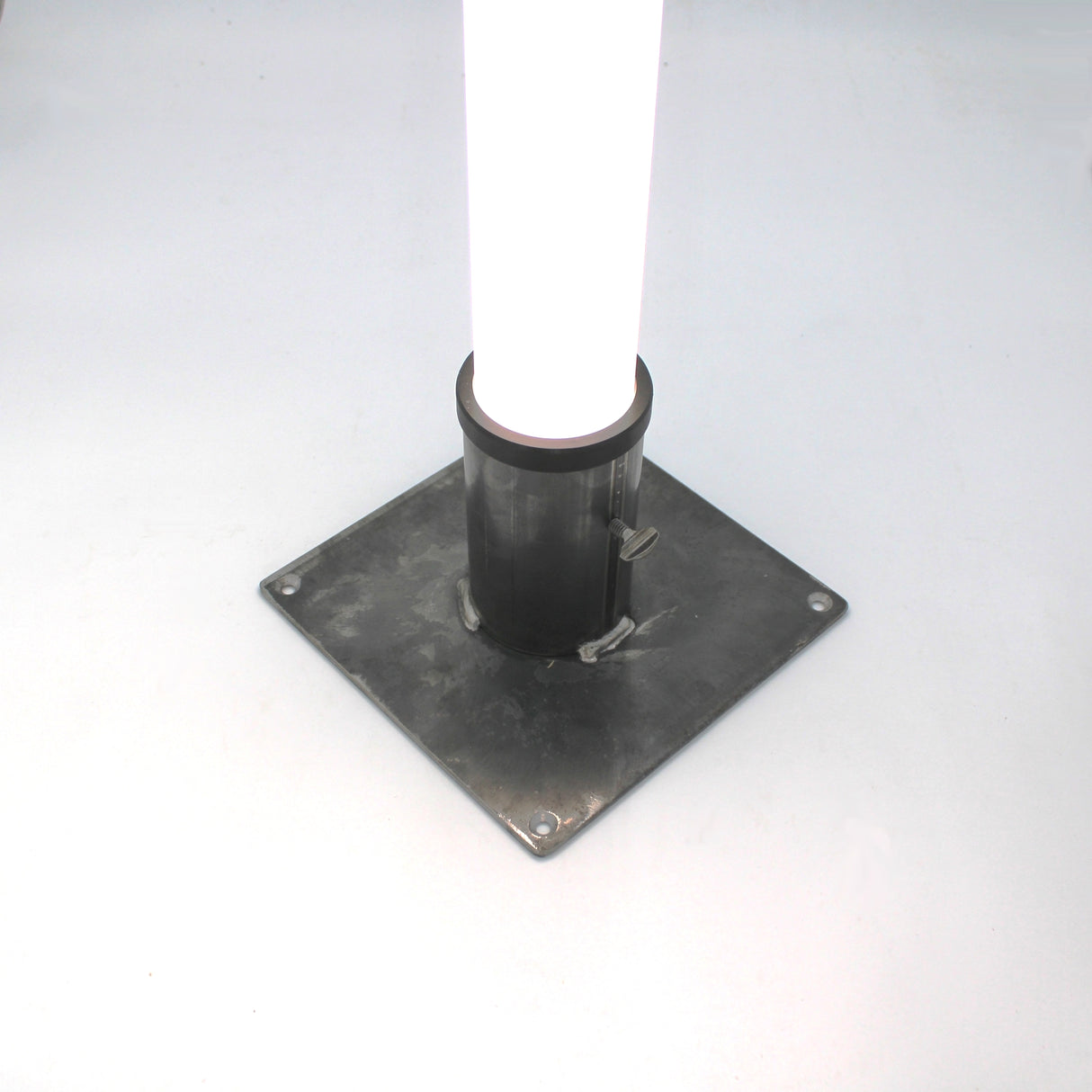 The Steel Base for 2.56" Round Profiles is a sturdy steel plate with four bolt holes, designed to mount a round diffuser tube vertically as a secure floor stand on flat surfaces.