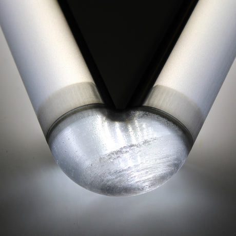 Close-up of the rounded, polished tip of the Translucent Elbow for Oslo Profile, featuring a V-shaped black and silver design above it, illuminated and casting a soft reflection on a white surface.