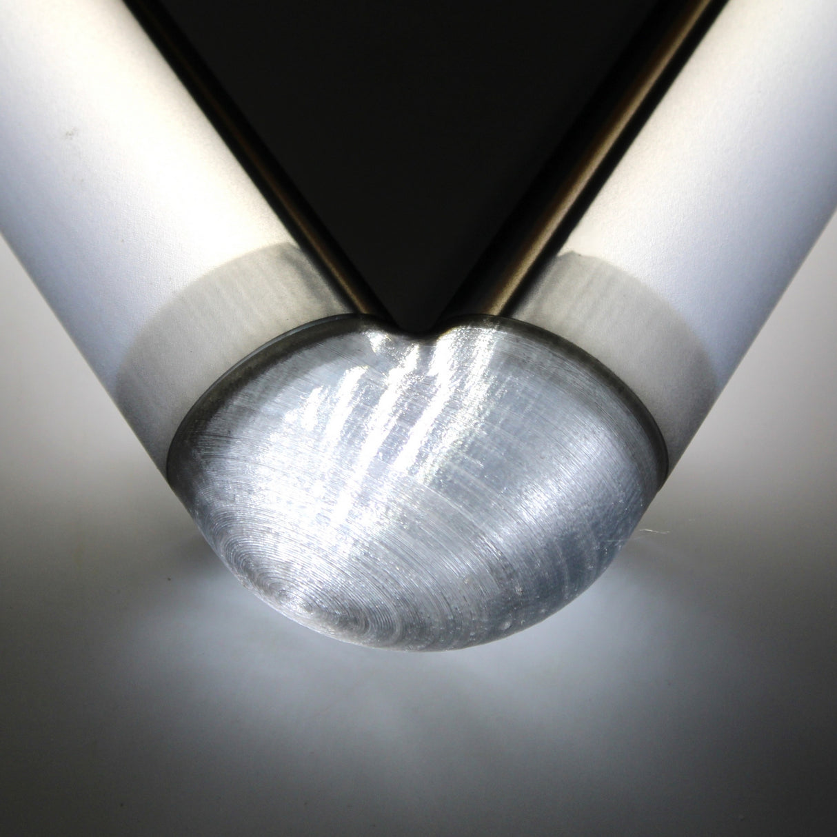 Close-up of a Translucent Elbow for Oslo Profile connecting two cylindrical rods at a right angle, with bright light reflecting off its polished surface.