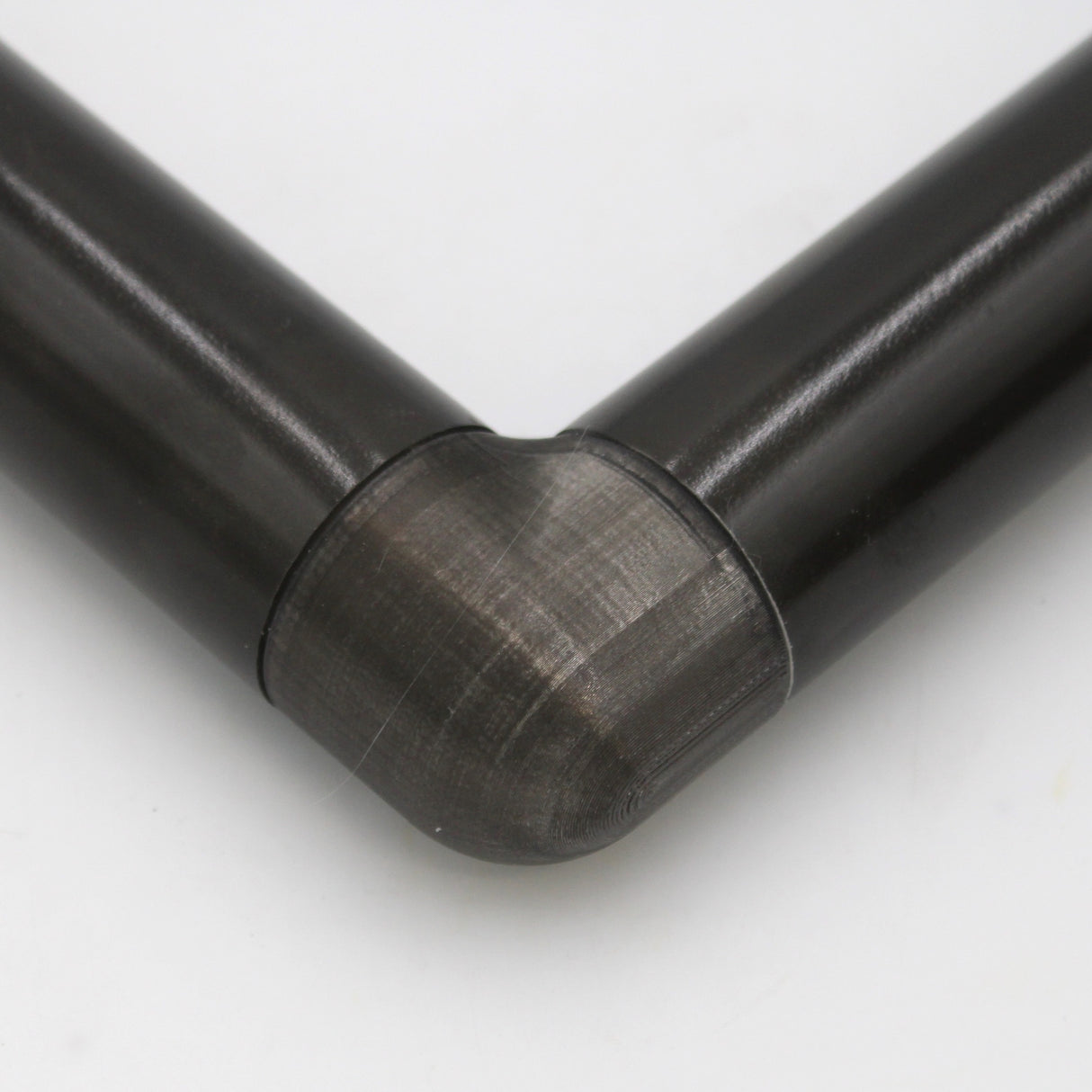 Close-up of two black cylindrical pipes joined at a right angle with a smooth, translucent Translucent Elbow for Oslo Profile connector against a white background.