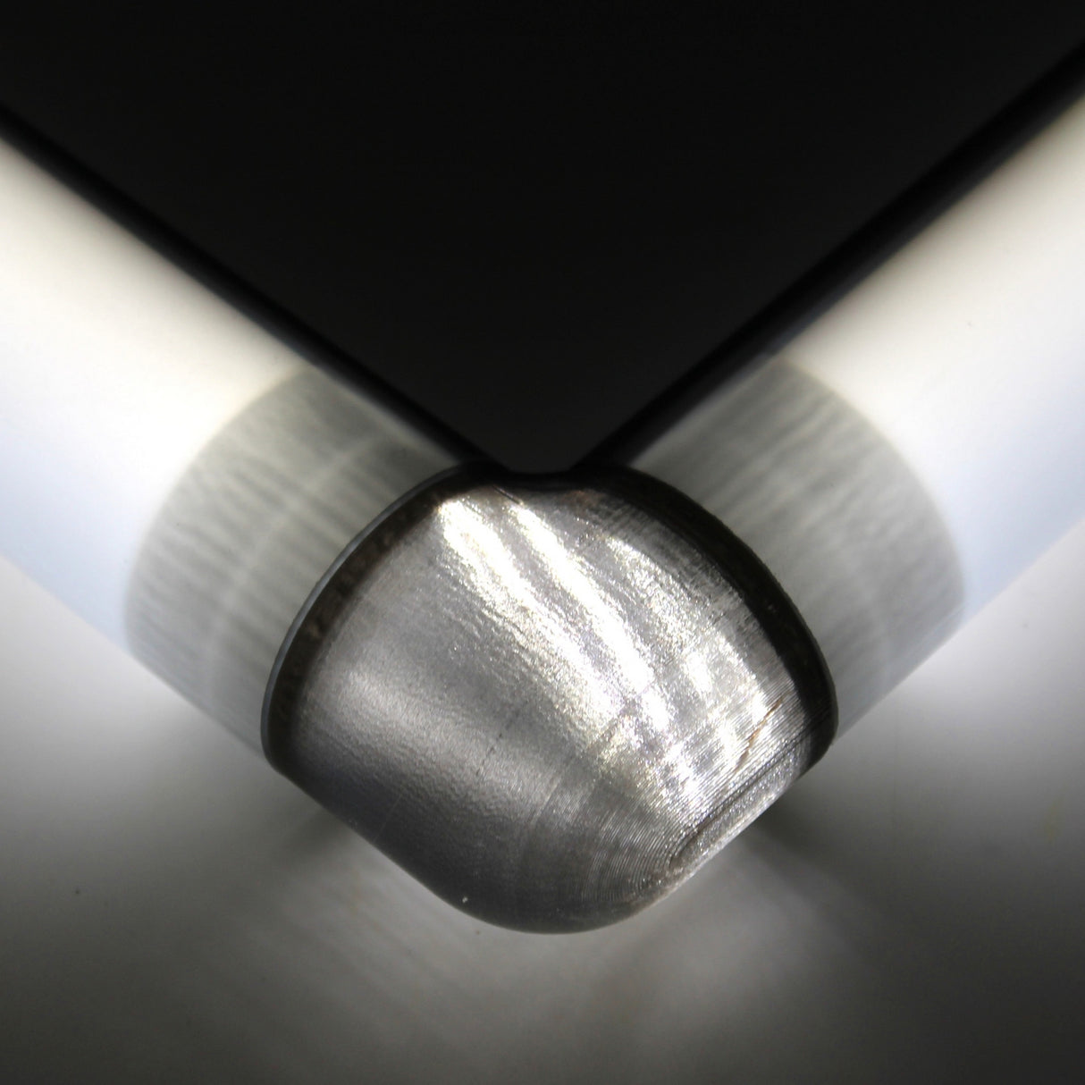 Close-up of a Translucent Elbow for Oslo Profile, featuring a rounded, brushed texture attached to a sleek black and white surface, integrating a 3D print joint and illuminated to emphasize its smooth, reflective finish.